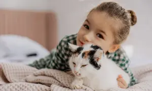 Mała dziewczynka przytula swojego kota. Ich więź jest widoczna, gdy kot wtula się w jej ramiona.